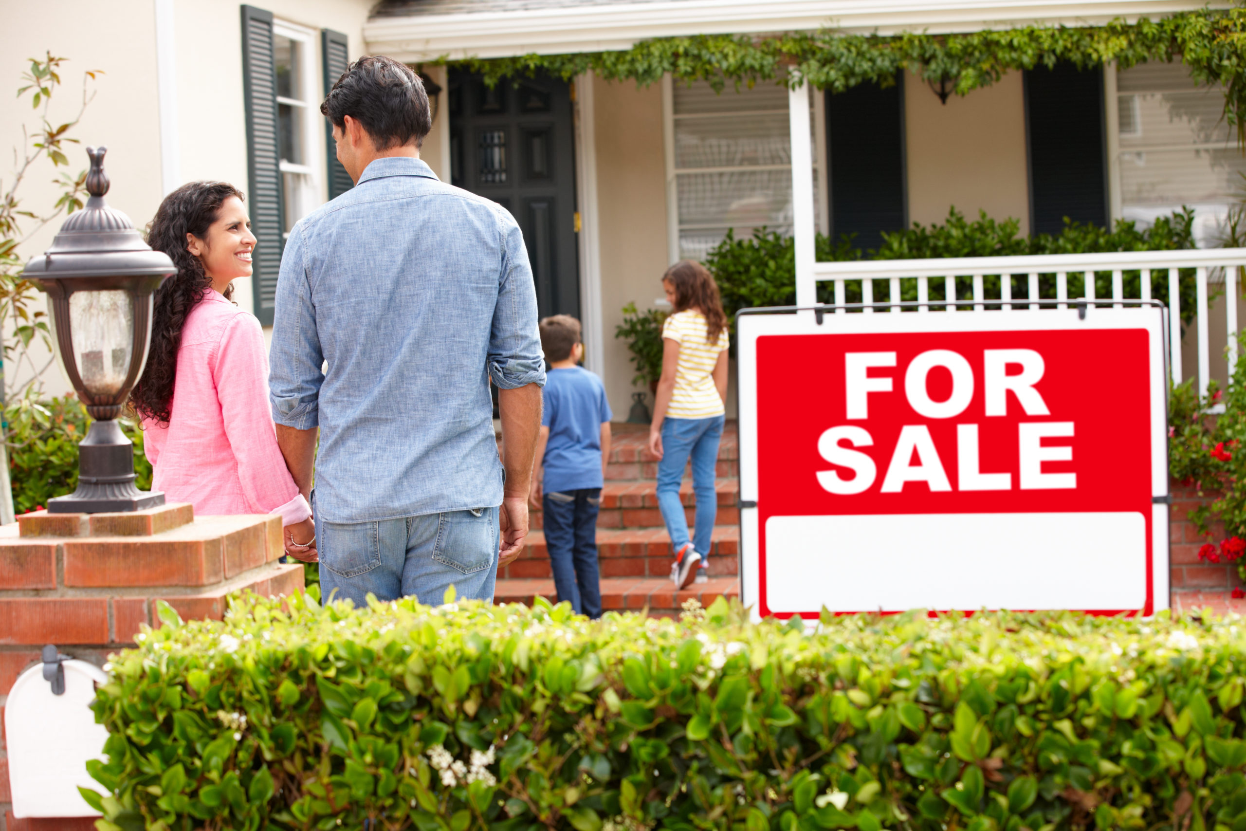 Hispanic family outside home with for sale sign